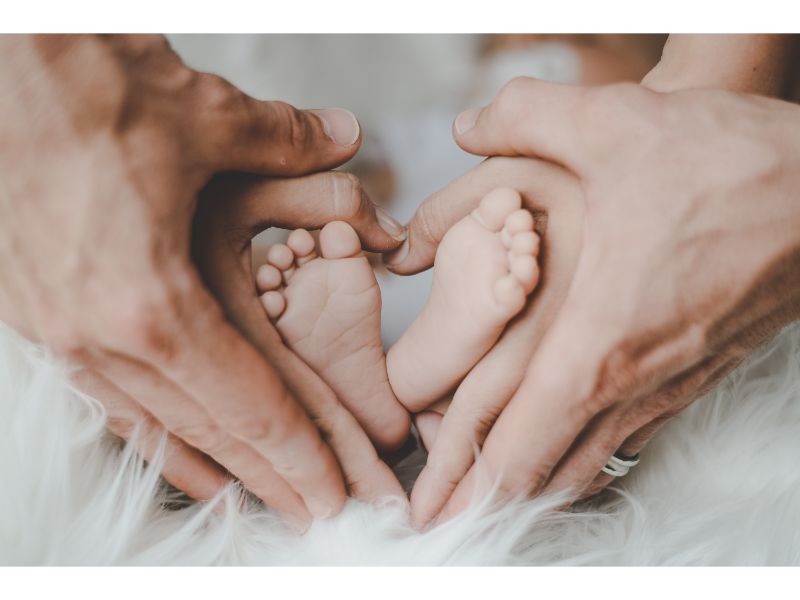赤ちゃんの足をハートに重なるように両親が手で包みこむ写真