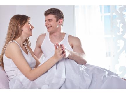 ベッドで手を重ねるカップルの写真