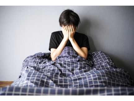 ベッドで顔を手で覆う男性の写真